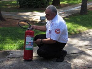 imagem mostra um instrutor de brigada de Incêndio, demonstrando os detalhes de um extintor de incêndio